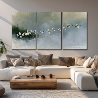A flock of white birds flying low above a quiet blue-green lake 3 piece canvas wall art displayed in a living room