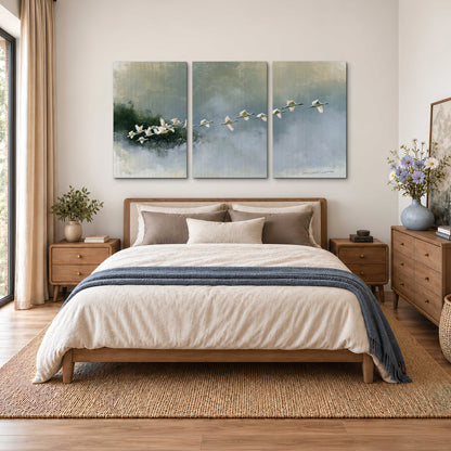 A flock of white birds flying low above a quiet blue-green lake 3 piece canvas wall art styled in an interior