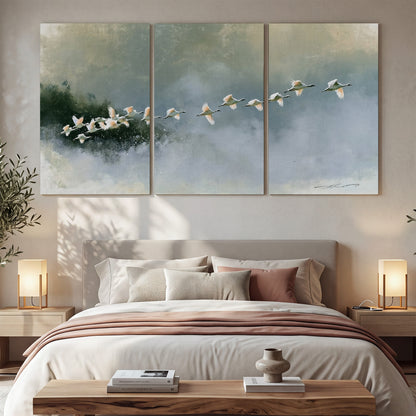 A flock of white birds flying low above a quiet blue-green lake 3 piece canvas wall art displayed in a bedroom