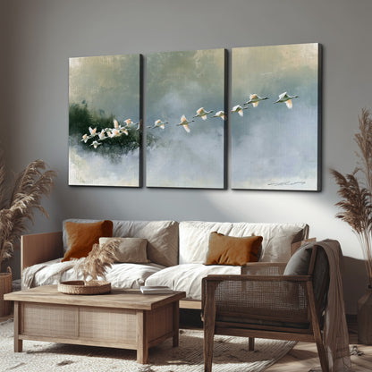 A flock of white birds flying low above a quiet blue-green lake 3 piece canvas wall art displayed in a rustic living room