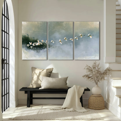A flock of white birds flying low above a quiet blue-green lake 3 piece canvas wall art displayed in a entryway