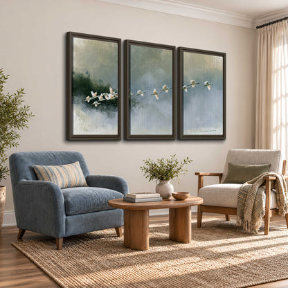 A flock of white birds flying low above a quiet blue-green lake 3 piece framed canvas wall art styled in an interior