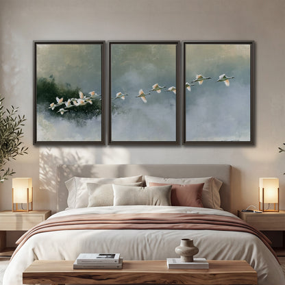 A flock of white birds flying low above a quiet blue-green lake 3 piece framed canvas wall art displayed in a bedroom