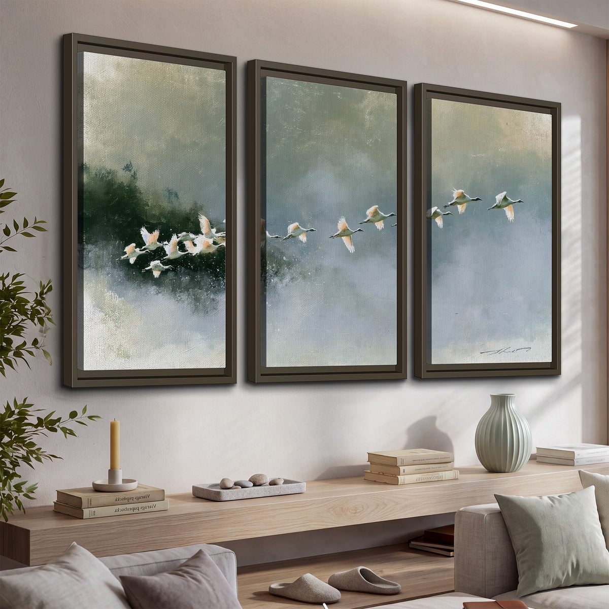 A flock of white birds flying low above a quiet blue-green lake 3 piece framed canvas wall art displayed in a console