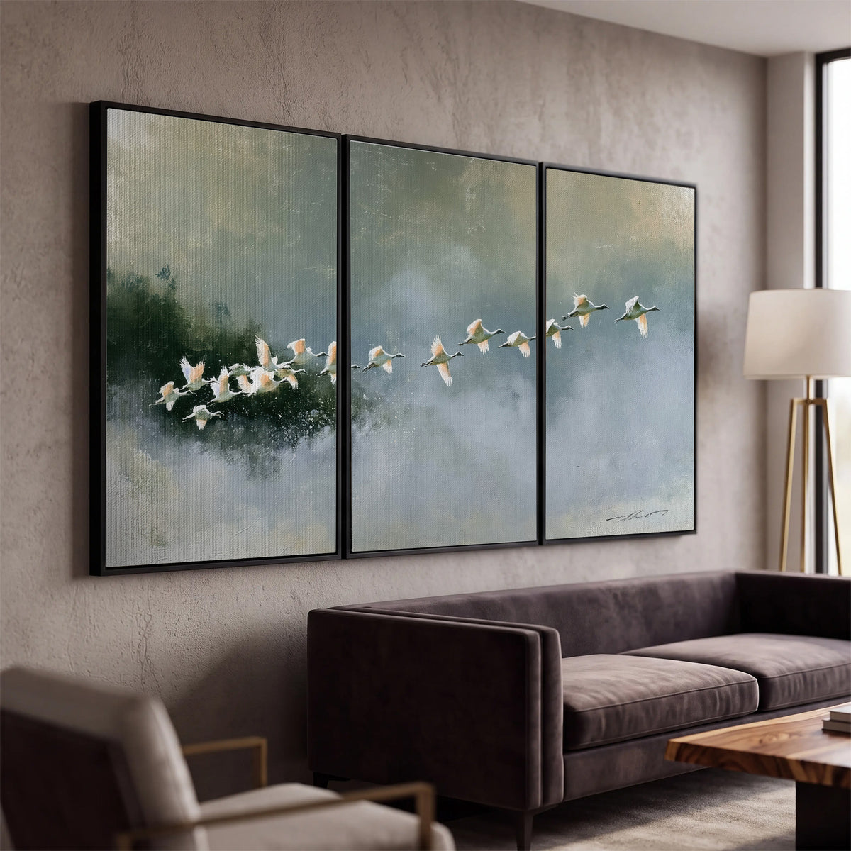 A flock of white birds flying low above a quiet blue-green lake 3 piece framed canvas wall art displayed in a modern living room