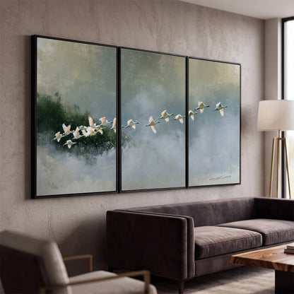 A flock of white birds flying low above a quiet blue-green lake 3 piece framed canvas wall art displayed in a modern living room