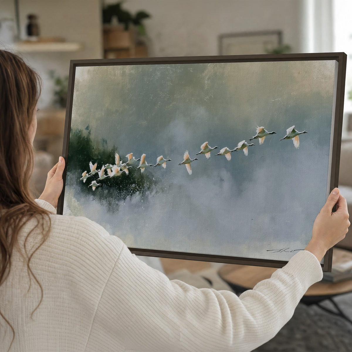 A flock of white birds flying low above a quiet blue-green lake single framed canvas wall art held in hands