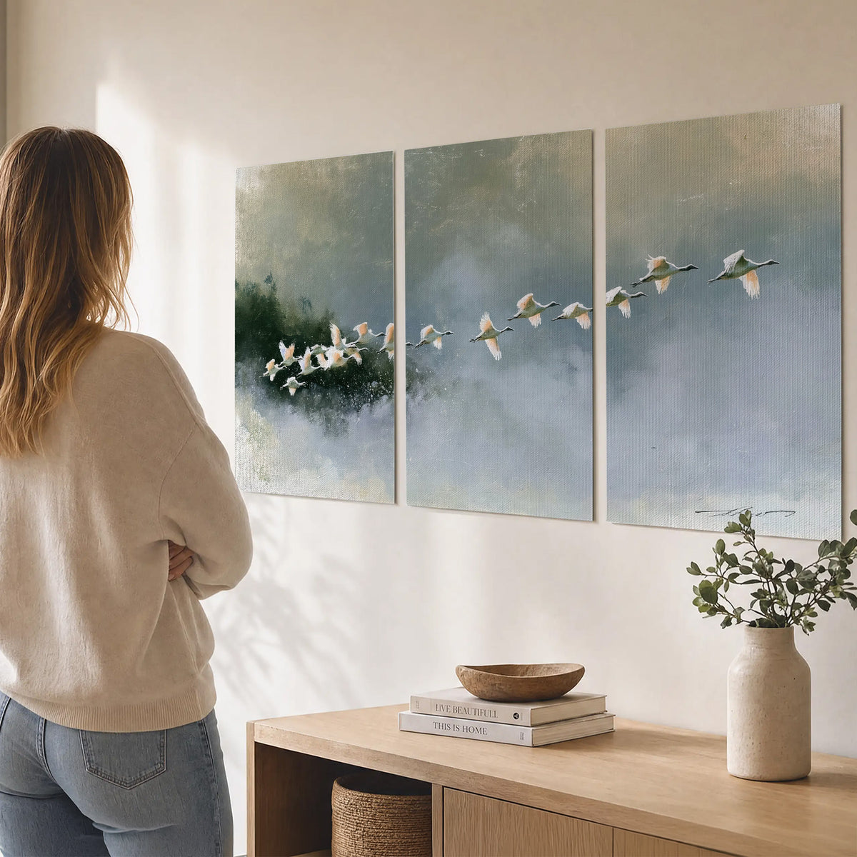A flock of white birds flying low above a quiet blue-green lake set of 3 poster prints three panel arrangement on a wall