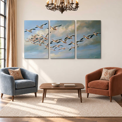 A flock of pale seabirds gliding beneath soft clouds across a blue sky 3 piece canvas wall art styled in an interior