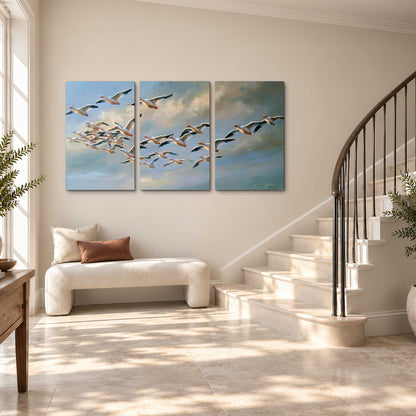 A flock of pale seabirds gliding beneath soft clouds across a blue sky 3 piece canvas wall art styled in an interior