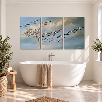 A flock of pale seabirds gliding beneath soft clouds across a blue sky 3 piece canvas wall art styled in an interior