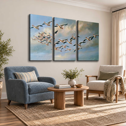 A flock of pale seabirds gliding beneath soft clouds across a blue sky 3 piece canvas wall art styled in an interior