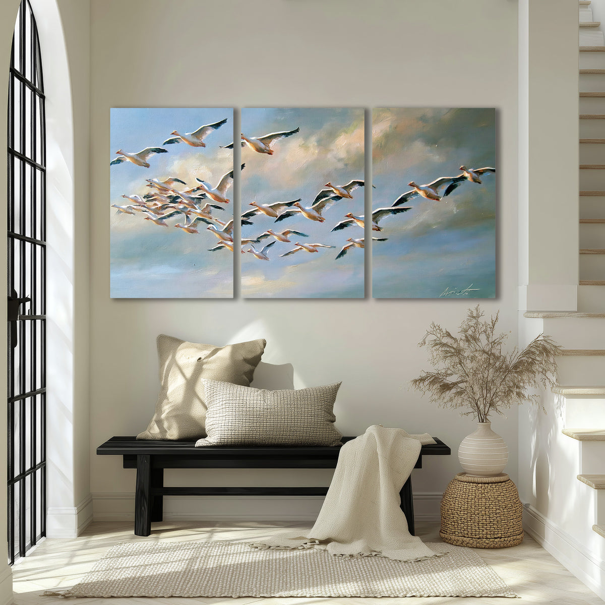 A flock of pale seabirds gliding beneath soft clouds across a blue sky 3 piece canvas wall art displayed in a entryway