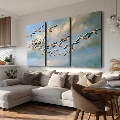 A flock of pale seabirds gliding beneath soft clouds across a blue sky 3 piece canvas wall art room and product view