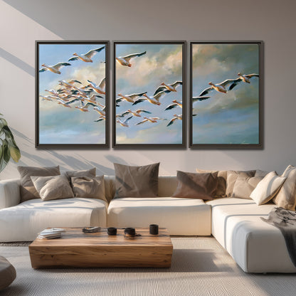 A flock of pale seabirds gliding beneath soft clouds across a blue sky 3 piece framed canvas wall art displayed in a living room