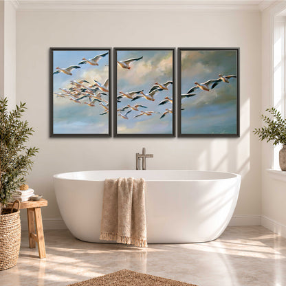 A flock of pale seabirds gliding beneath soft clouds across a blue sky 3 piece framed canvas wall art styled in an interior
