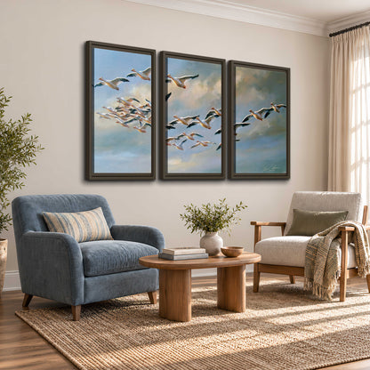 A flock of pale seabirds gliding beneath soft clouds across a blue sky 3 piece framed canvas wall art styled in an interior