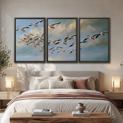 A flock of pale seabirds gliding beneath soft clouds across a blue sky 3 piece framed canvas wall art displayed in a bedroom