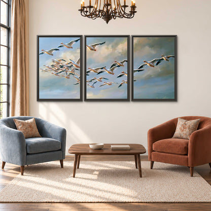 A flock of pale seabirds gliding beneath soft clouds across a blue sky 3 piece framed canvas wall art styled in an interior