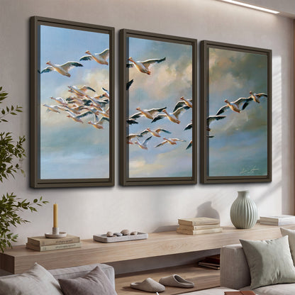 A flock of pale seabirds gliding beneath soft clouds across a blue sky 3 piece framed canvas wall art displayed in a console