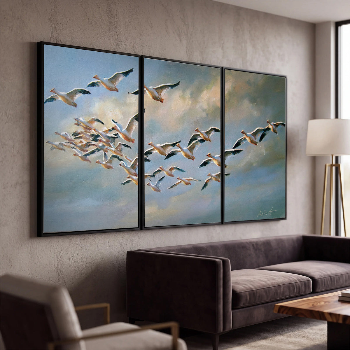 A flock of pale seabirds gliding beneath soft clouds across a blue sky 3 piece framed canvas wall art displayed in a modern living room