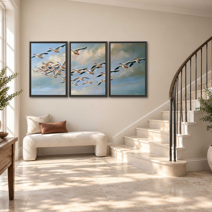 A flock of pale seabirds gliding beneath soft clouds across a blue sky 3 piece framed canvas wall art styled in an interior