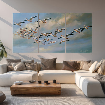 A flock of pale seabirds gliding beneath soft clouds across a blue sky set of 3 poster prints displayed in a living room