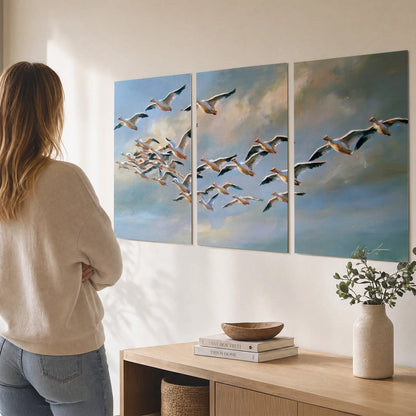 A flock of pale seabirds gliding beneath soft clouds across a blue sky set of 3 poster prints three panel arrangement on a wall