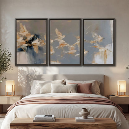 Pale bird-like forms sweeping across layered strokes of blue, ochre and cream 3 piece framed canvas wall art displayed in a bedroom