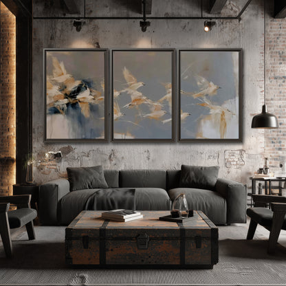 Pale bird-like forms sweeping across layered strokes of blue, ochre and cream 3 piece framed canvas wall art displayed in a industrial room