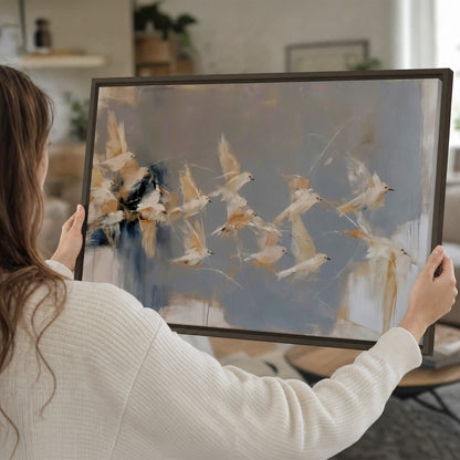Pale bird-like forms sweeping across layered strokes of blue, ochre and cream single framed canvas wall art held in hands