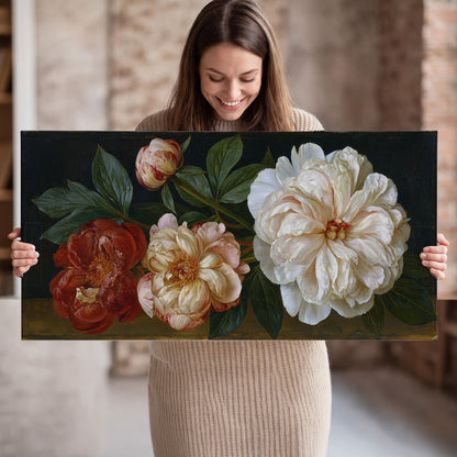 A large pale peony beside small ruby-red and peach flowers on a deep green ground single canvas wall art held in hands