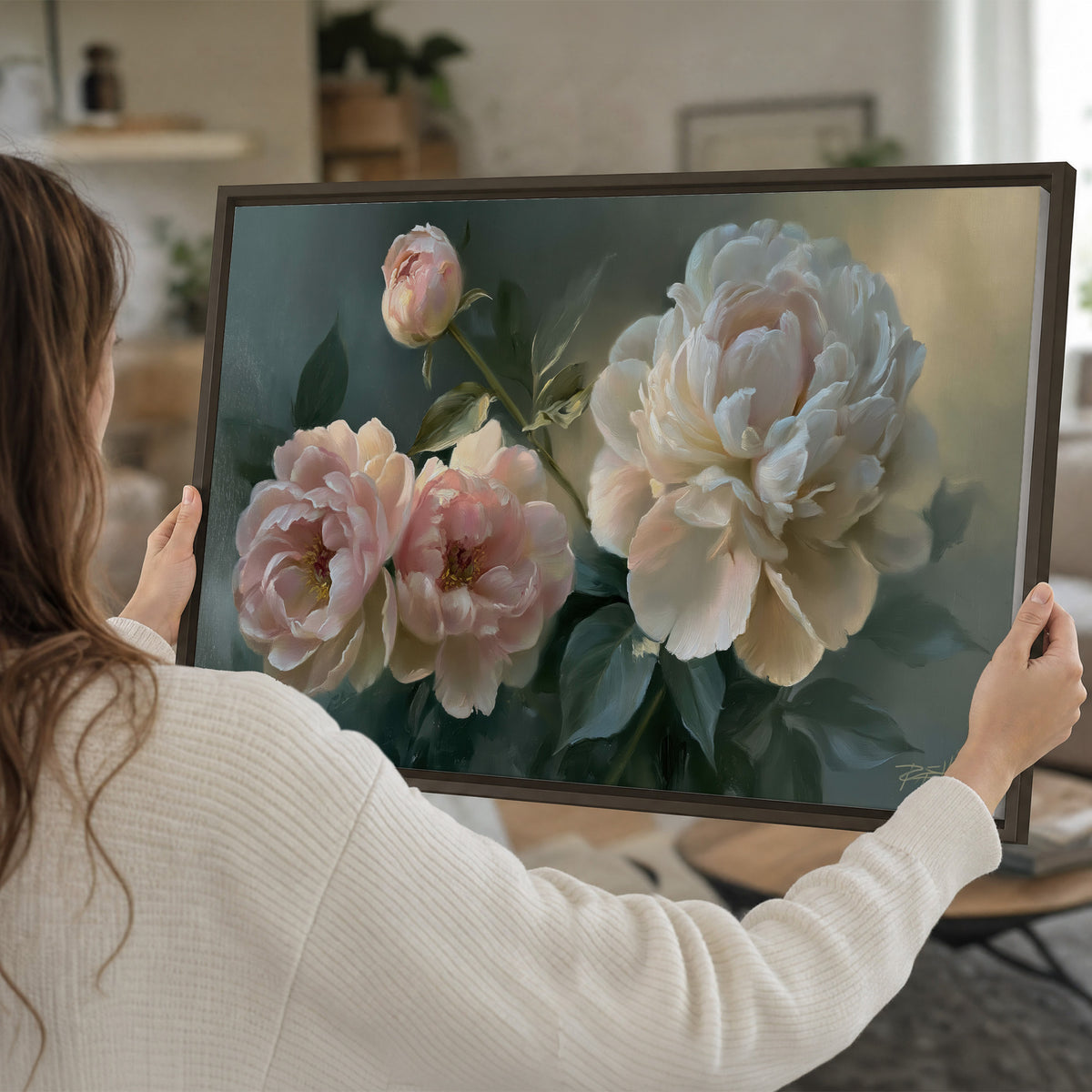 A large cream peony beside blush flowers and broad green leaves single framed canvas wall art held in hands