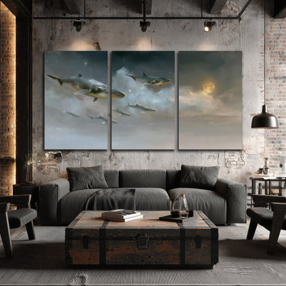 Whales drifting through pale dreamlike clouds toward a golden moon 3 piece canvas wall art displayed in a industrial room