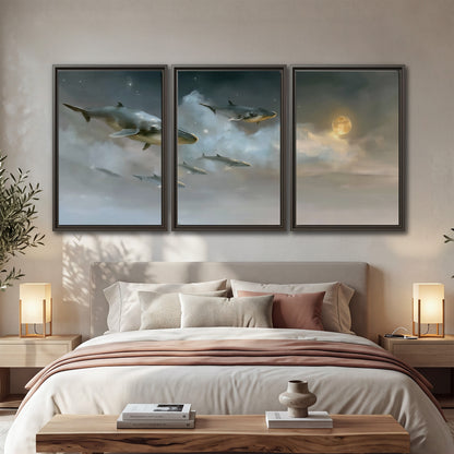 Whales drifting through pale dreamlike clouds toward a golden moon 3 piece framed canvas wall art displayed in a bedroom