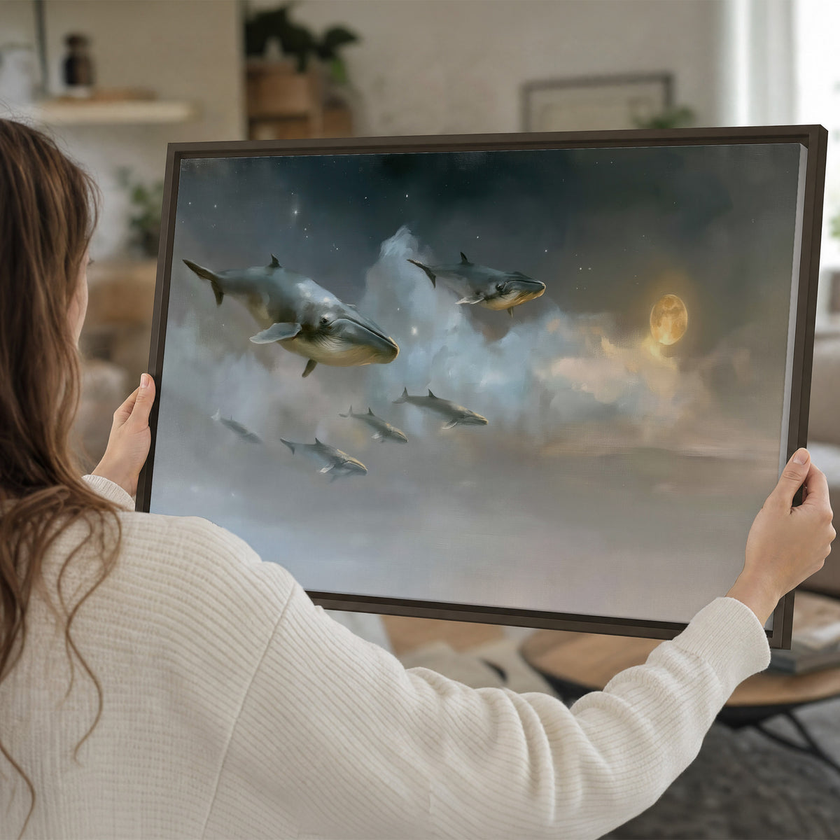 Whales drifting through pale dreamlike clouds toward a golden moon single framed canvas wall art held in hands