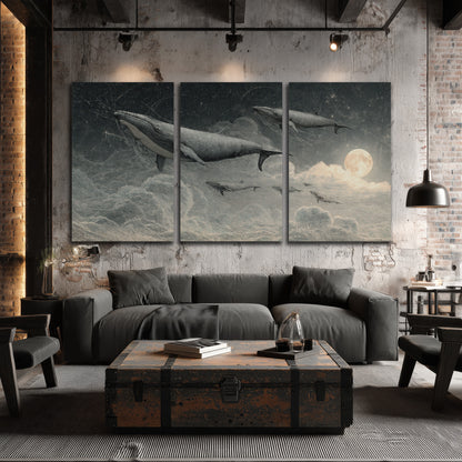 Monochrome whales floating over misty clouds beside a luminous painted moon 3 piece canvas wall art displayed in a industrial room