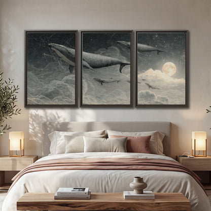 Monochrome whales floating over misty clouds beside a luminous painted moon 3 piece framed canvas wall art displayed in a bedroom