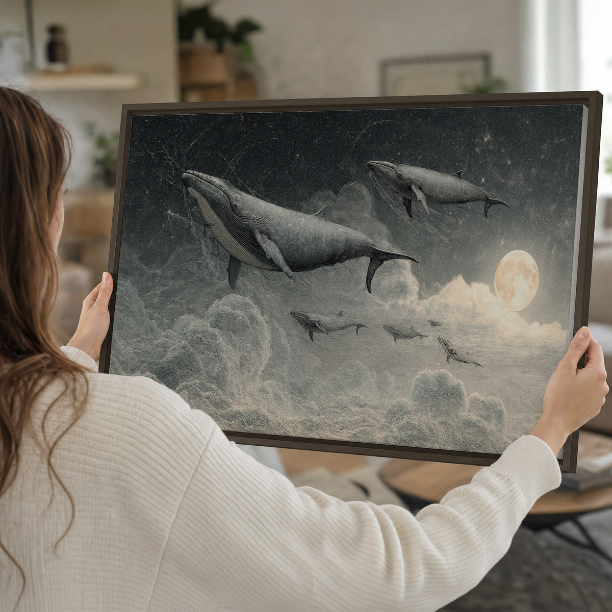 Monochrome whales floating over misty clouds beside a luminous painted moon single framed canvas wall art held in hands