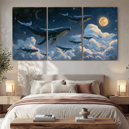 A group of whales floating among clouds beneath a golden moon in a deep blue night sky 3 piece canvas wall art displayed in a bedroom