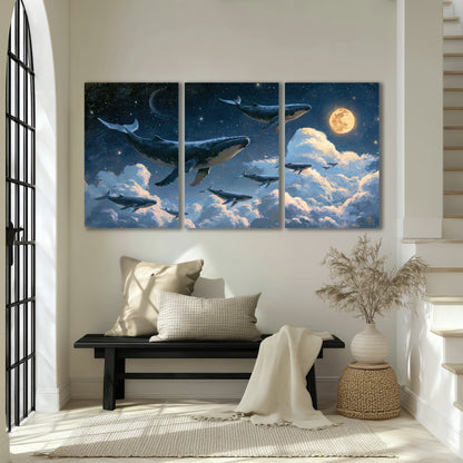 A group of whales floating among clouds beneath a golden moon in a deep blue night sky 3 piece canvas wall art displayed in a entryway