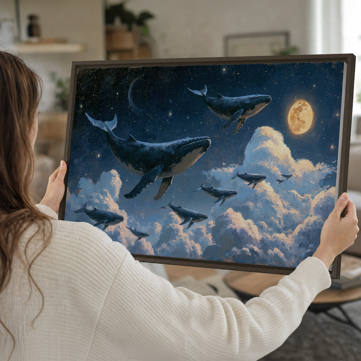 A group of whales floating among clouds beneath a golden moon in a deep blue night sky single framed canvas wall art held in hands