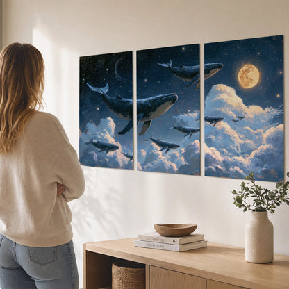 A group of whales floating among clouds beneath a golden moon in a deep blue night sky set of 3 poster prints three panel arrangement on a wall