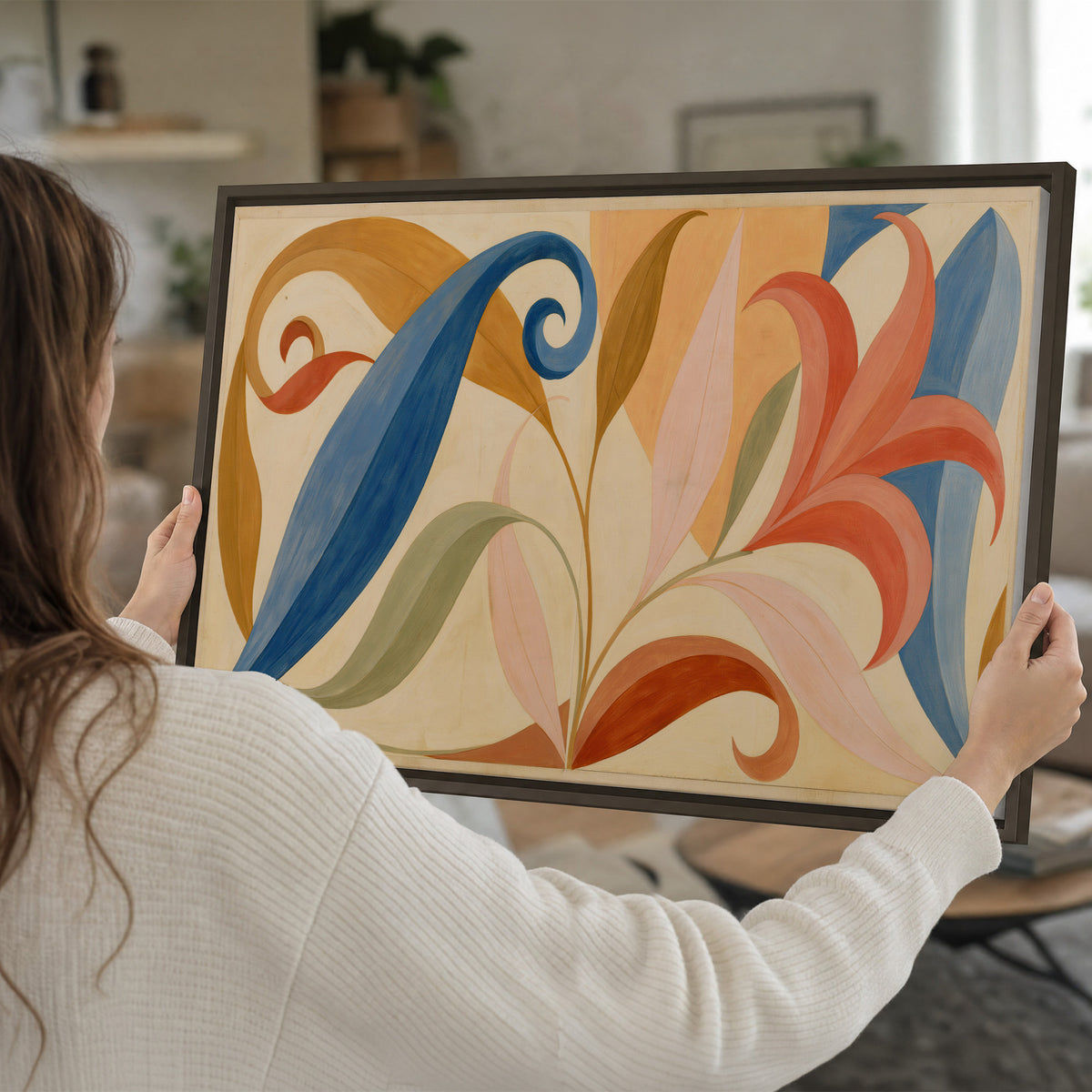Bold blue, coral and golden leaf-like shapes flowing across a cream ground single framed canvas wall art held in hands