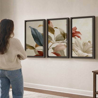 Cream flowers with broad blue and rust leaves sweeping across a neutral background 3 piece framed canvas wall art three panel arrangement on a wall