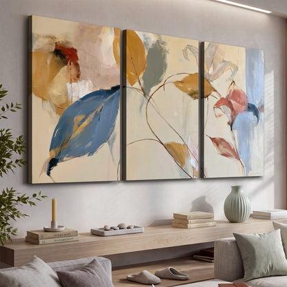 Loose ochre, blue and pink leaves arranged on a pale layered background 3 piece canvas wall art displayed in a console