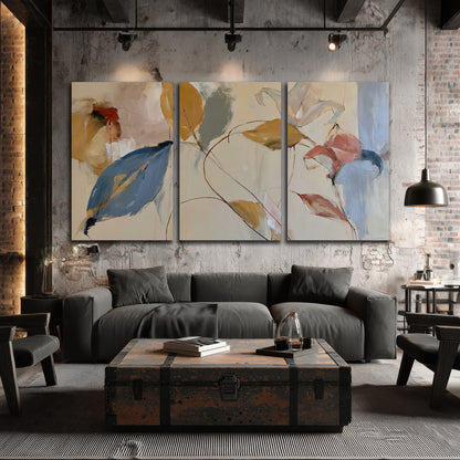 Loose ochre, blue and pink leaves arranged on a pale layered background 3 piece canvas wall art displayed in a industrial room