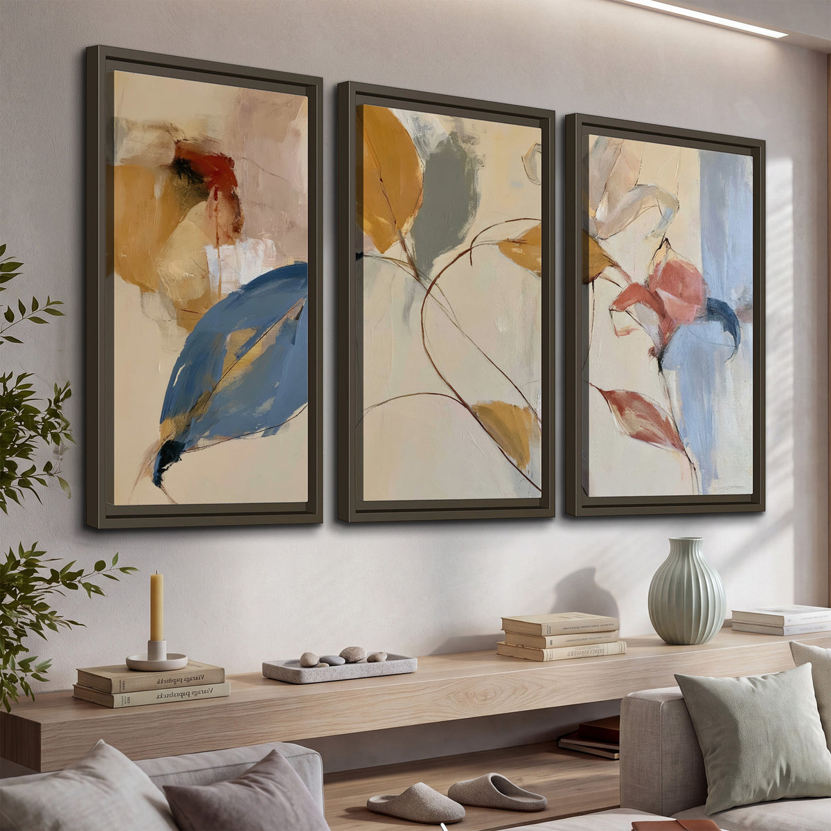 Loose ochre, blue and pink leaves arranged on a pale layered background 3 piece framed canvas wall art displayed in a console