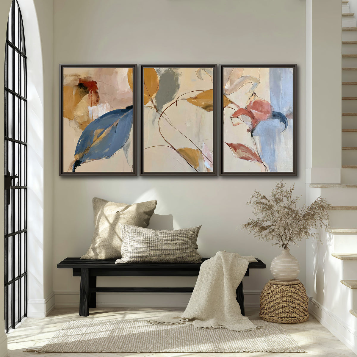 Loose ochre, blue and pink leaves arranged on a pale layered background 3 piece framed canvas wall art displayed in a entryway
