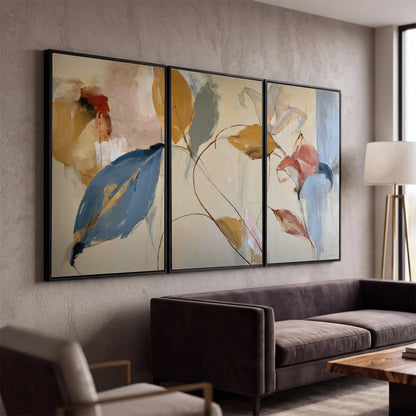 Loose ochre, blue and pink leaves arranged on a pale layered background 3 piece framed canvas wall art displayed in a modern living room